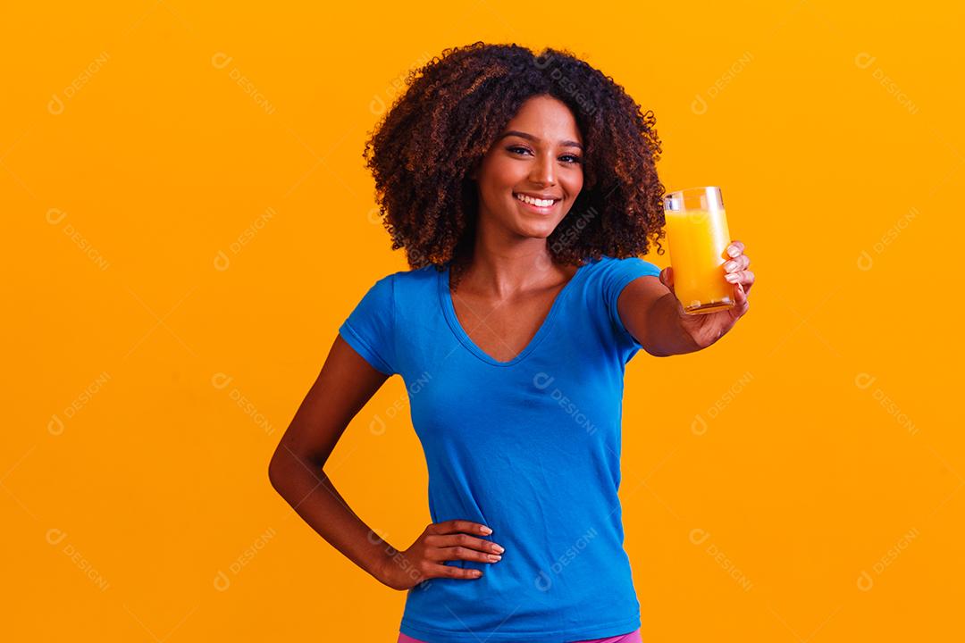 Mulher afro-americana bebendo suco de laranja em fundo amarelo