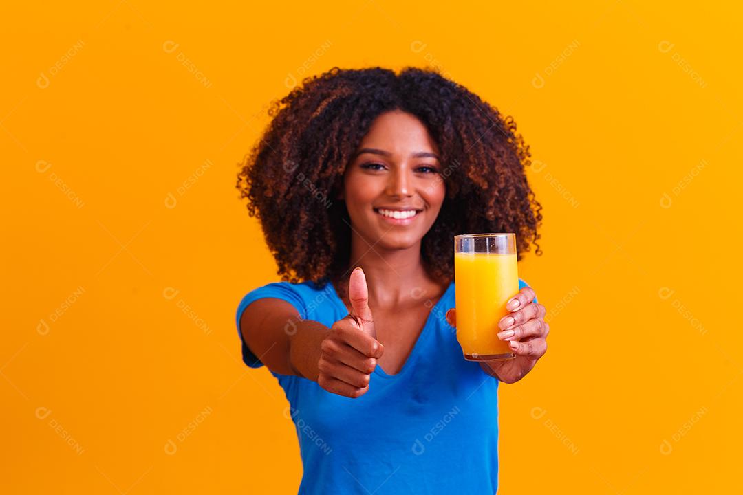 Mulher afro-americana bebendo suco de laranja em fundo amarelo
