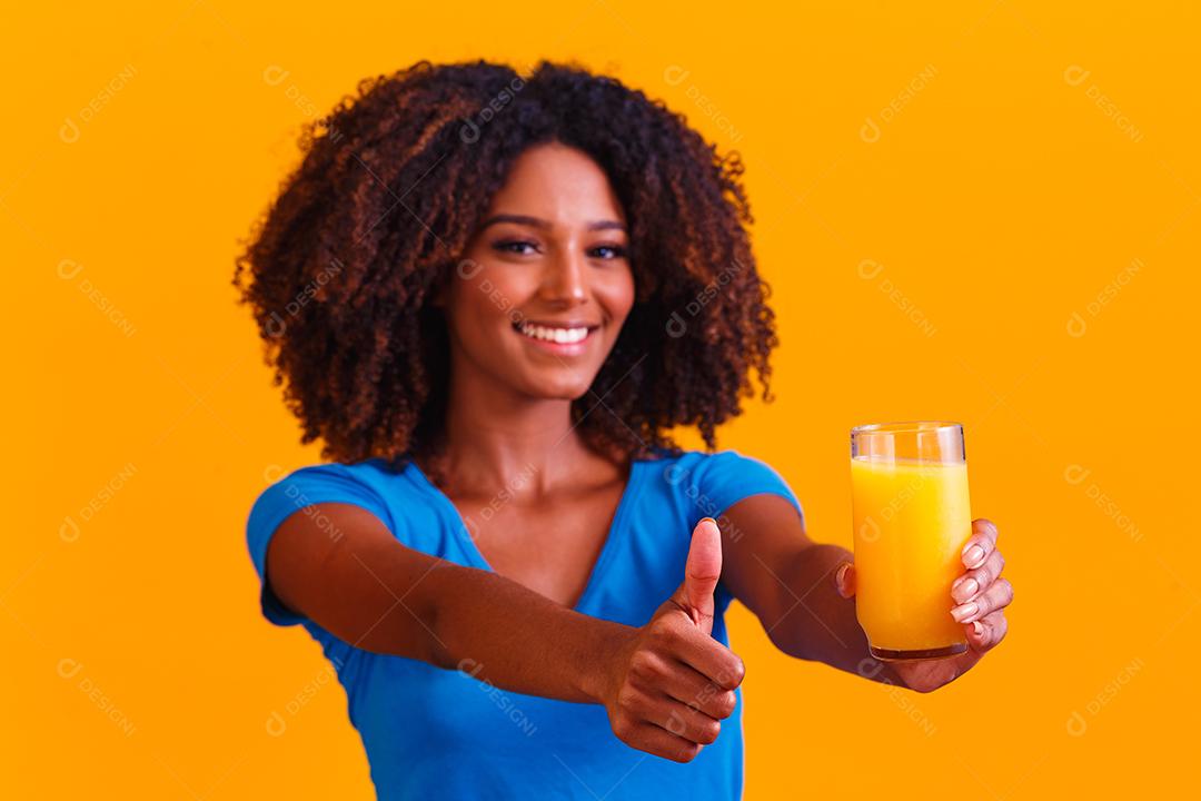 Mulher afro-americana bebendo suco de laranja em fundo amarelo