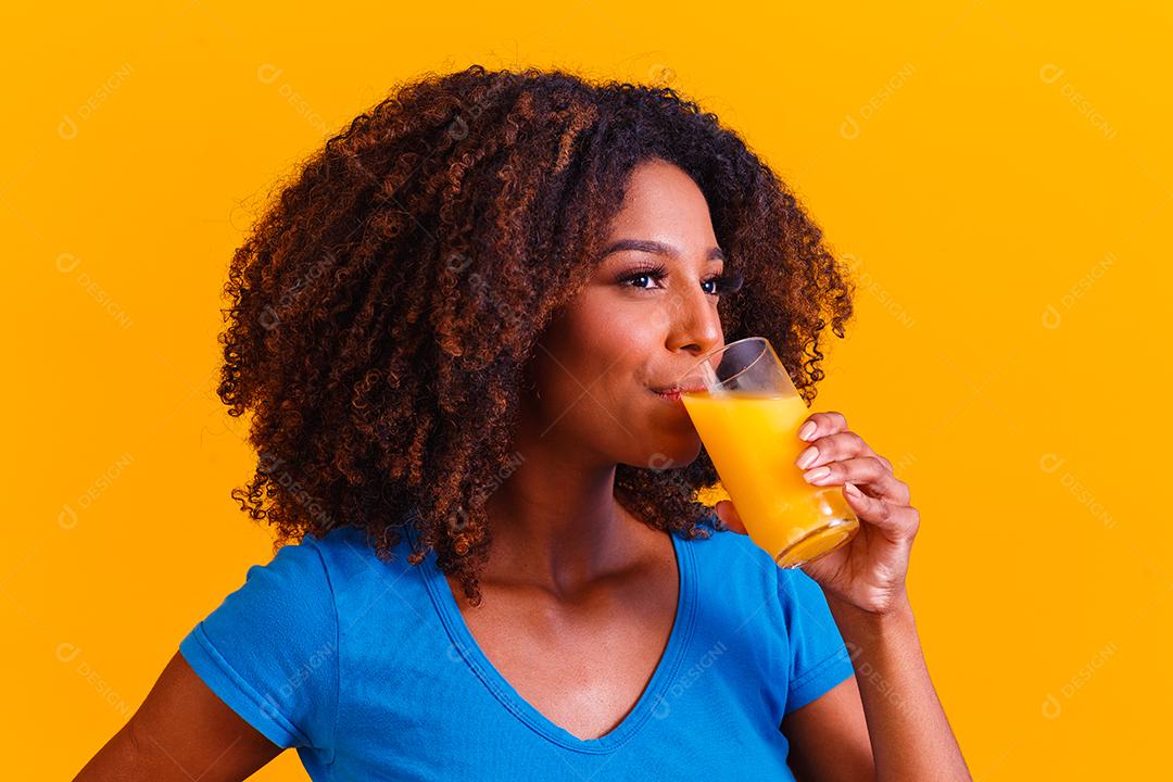 Mulher afro-americana bebendo suco de laranja em fundo amarelo