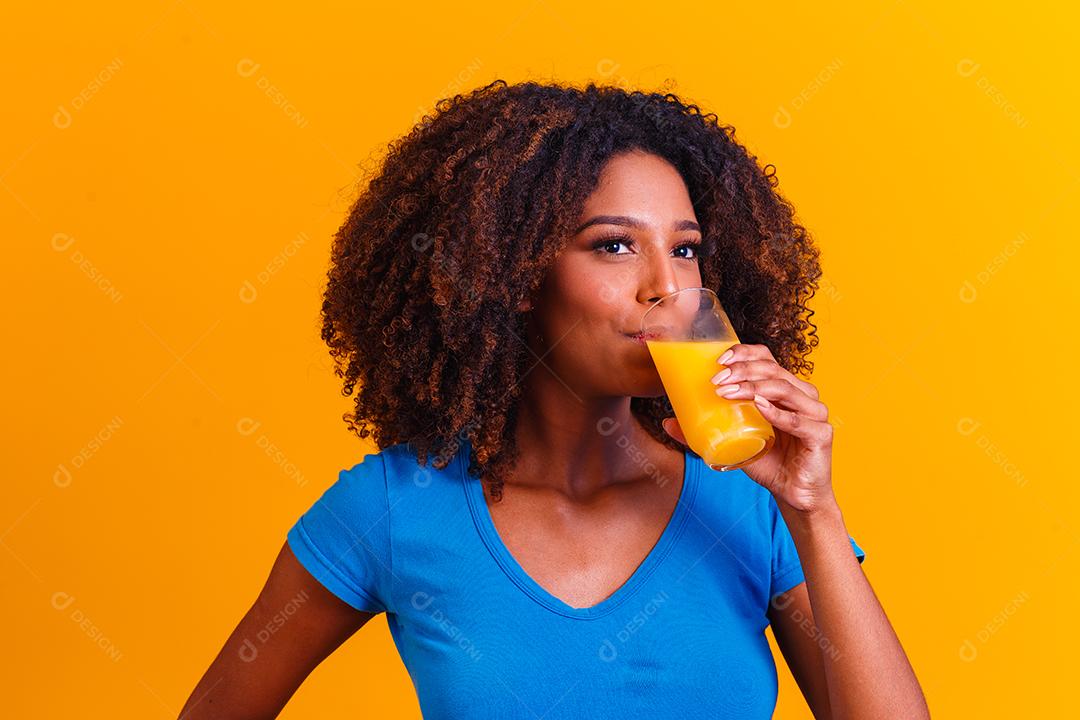 Mulher afro-americana bebendo suco de laranja em fundo amarelo