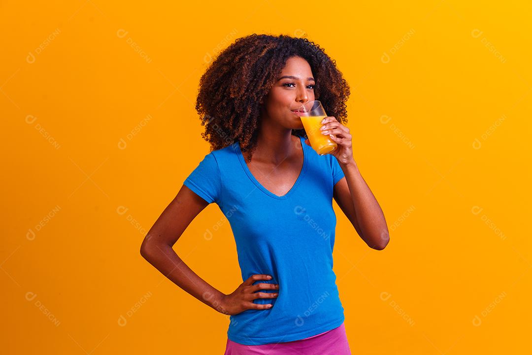 Mulher afro-americana bebendo suco de laranja em fundo amarelo