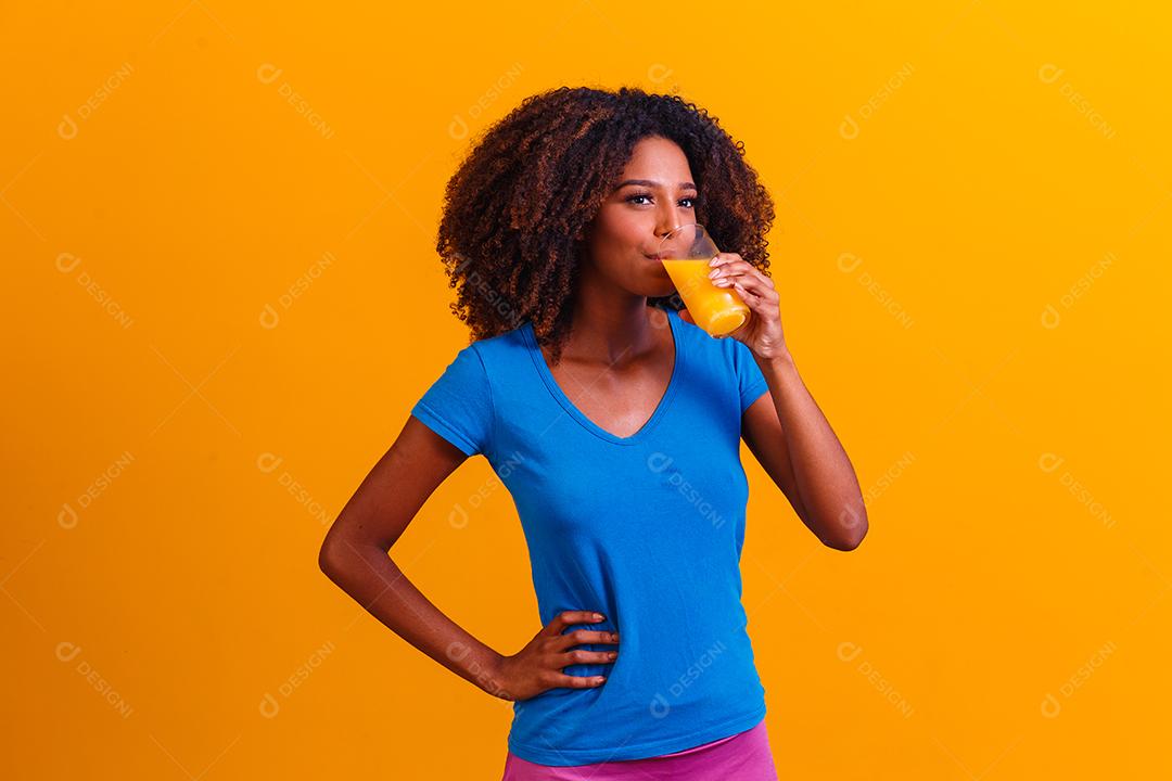 Mulher afro-americana bebendo suco de laranja em fundo amarelo