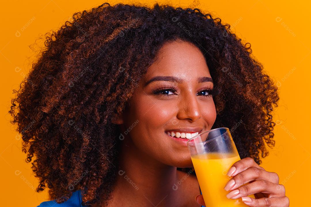 Mulher afro-americana bebendo suco de laranja em fundo amarelo