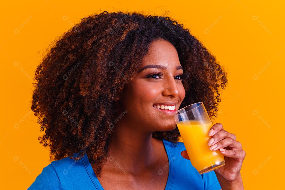 Mulher afro-americana bebendo suco de laranja em fundo amarelo