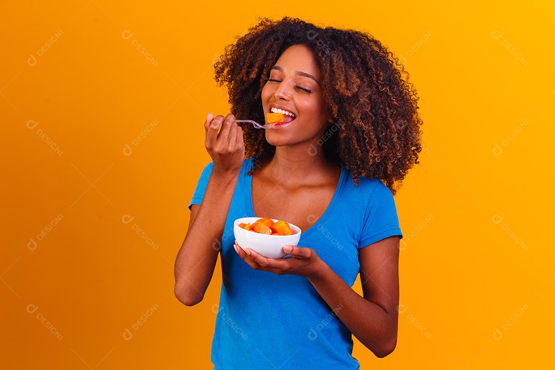 garota afro comendo mamão da tigela. Conceito de alimentação saudável