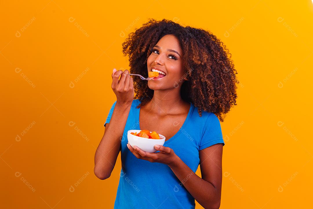 garota afro comendo mamão da tigela. Conceito de alimentação saudável