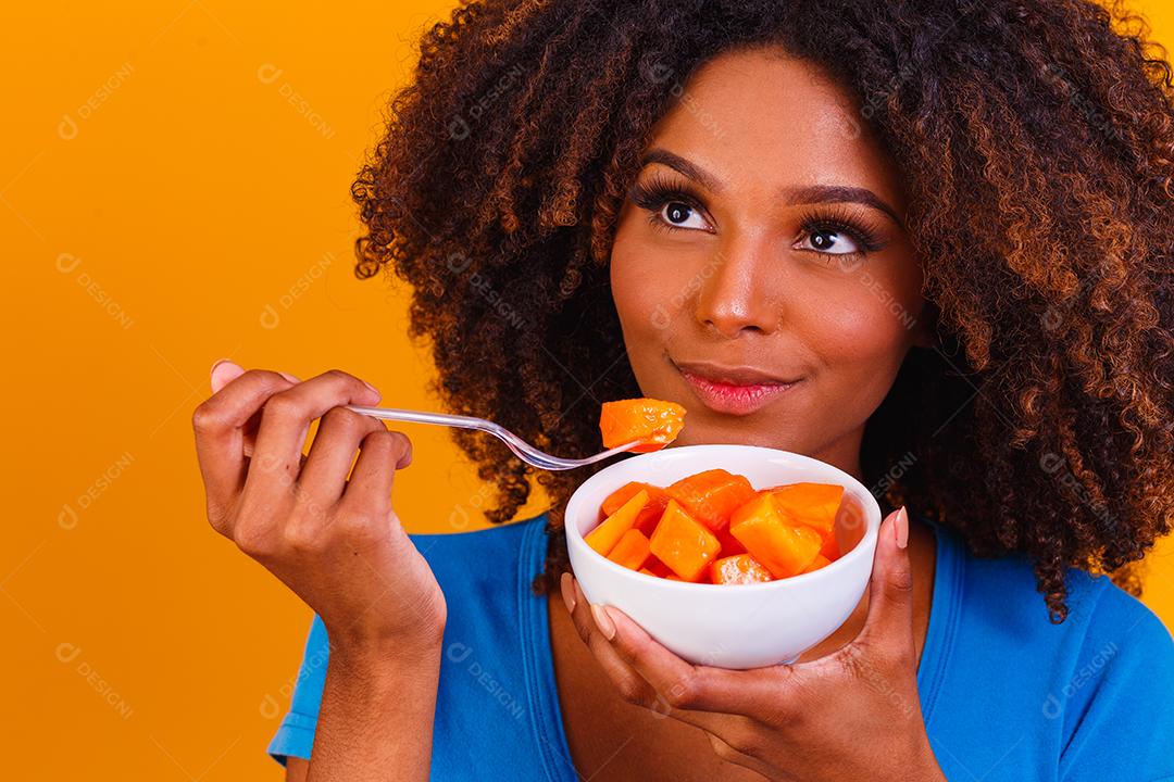 garota afro comendo mamão da tigela. Conceito de alimentação saudável
