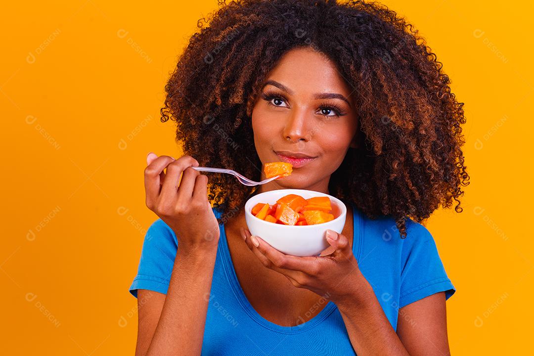 garota afro comendo mamão da tigela. Conceito de alimentação saudável