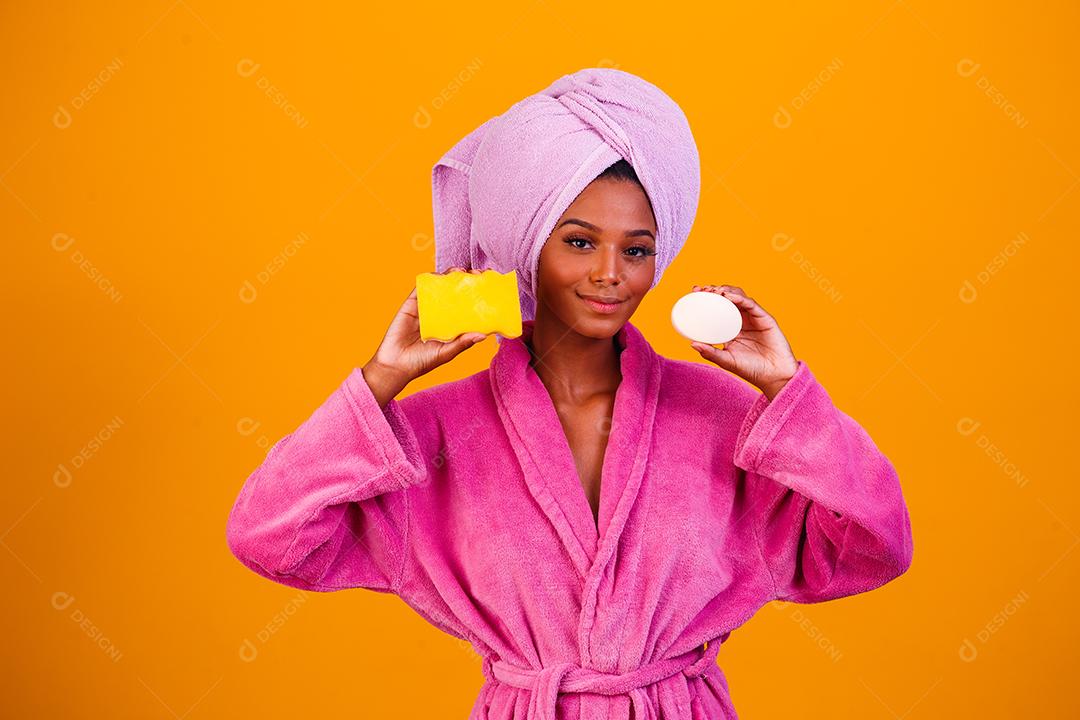 Linda Mulher Afro com Toalha na Cabeça e Roupão de Banho segurando Esponja e Sabonete