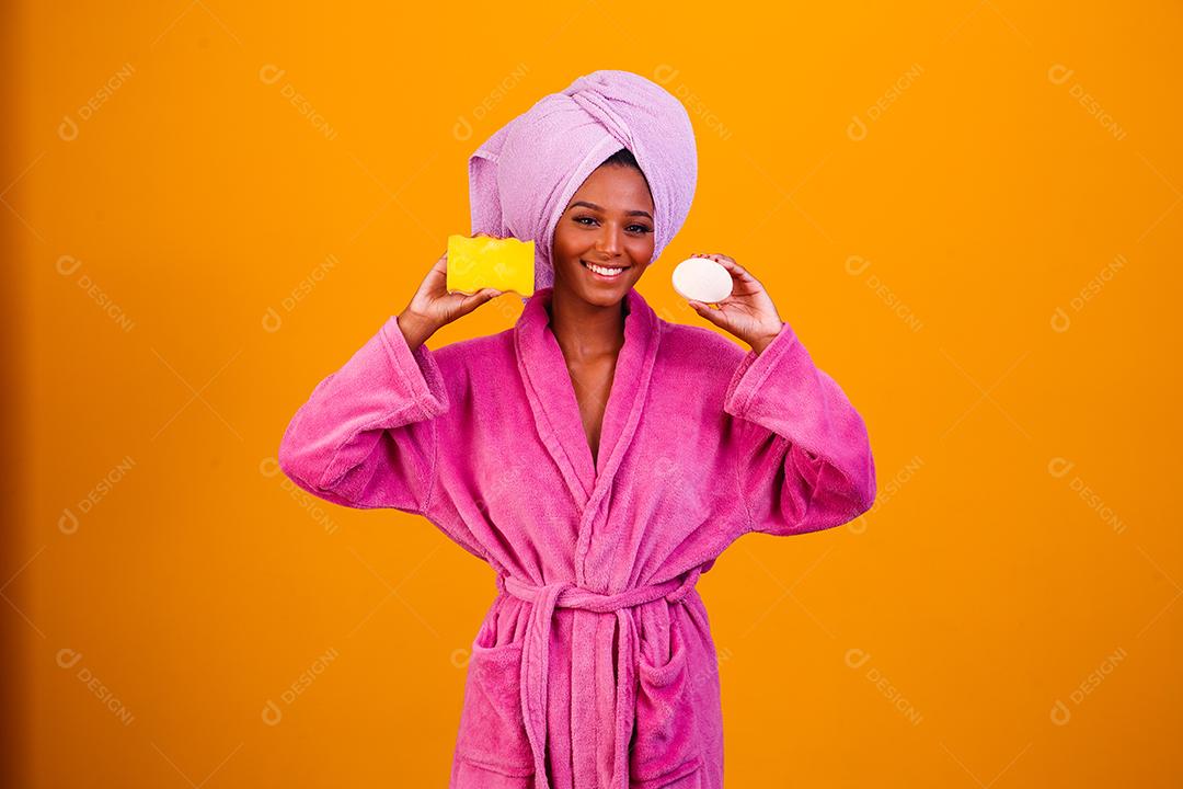 Linda Mulher Afro com Toalha na Cabeça e Roupão de Banho segurando Esponja e Sabonete