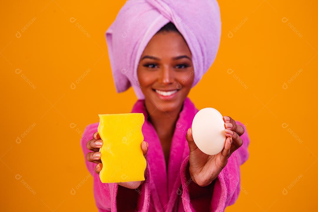 Linda Mulher Afro com Toalha na Cabeça e Roupão de Banho segurando Esponja e Sabonete