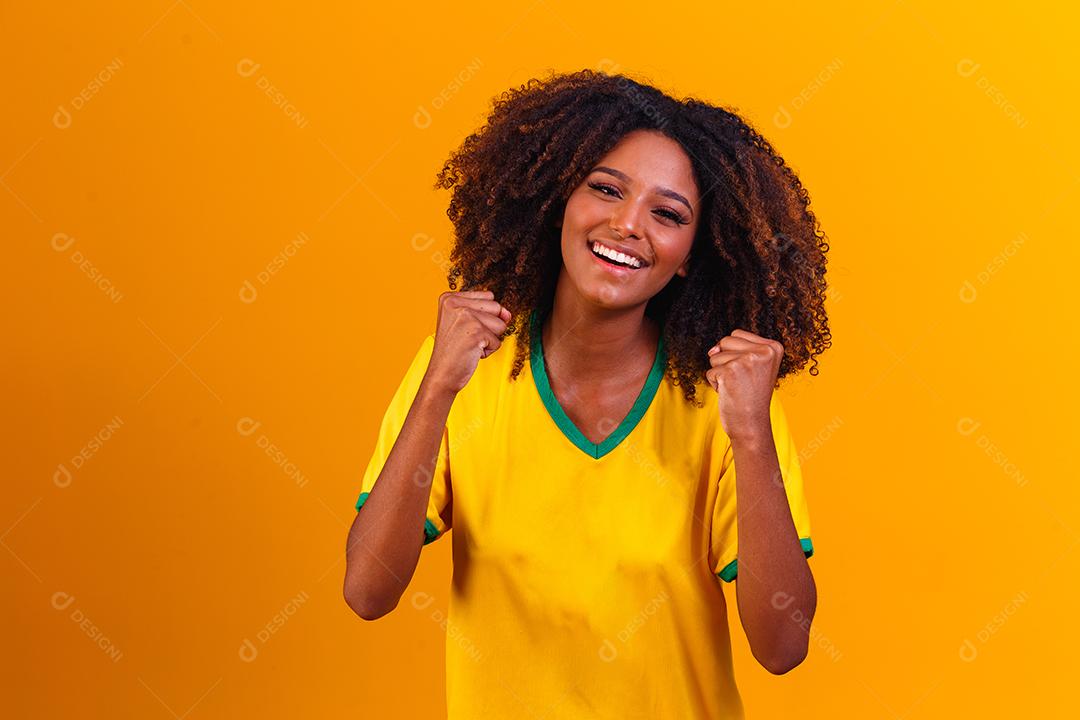torcedor brasileiro. Fã de mulher brasileira comemorando no futebol ou partida de futebol em fundo amarelo. Cores do Brasil.