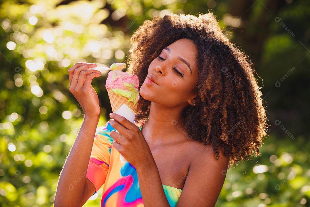 Mulher afro feliz tomando sorvete no parque.