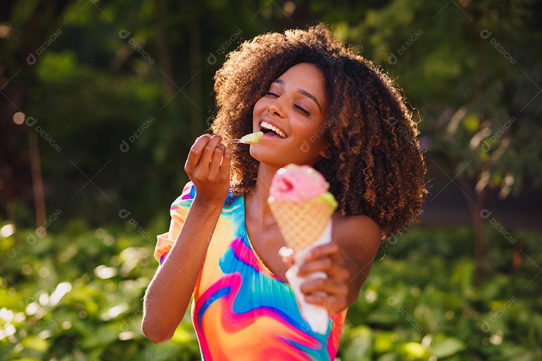 Mulher afro feliz tomando sorvete no parque.