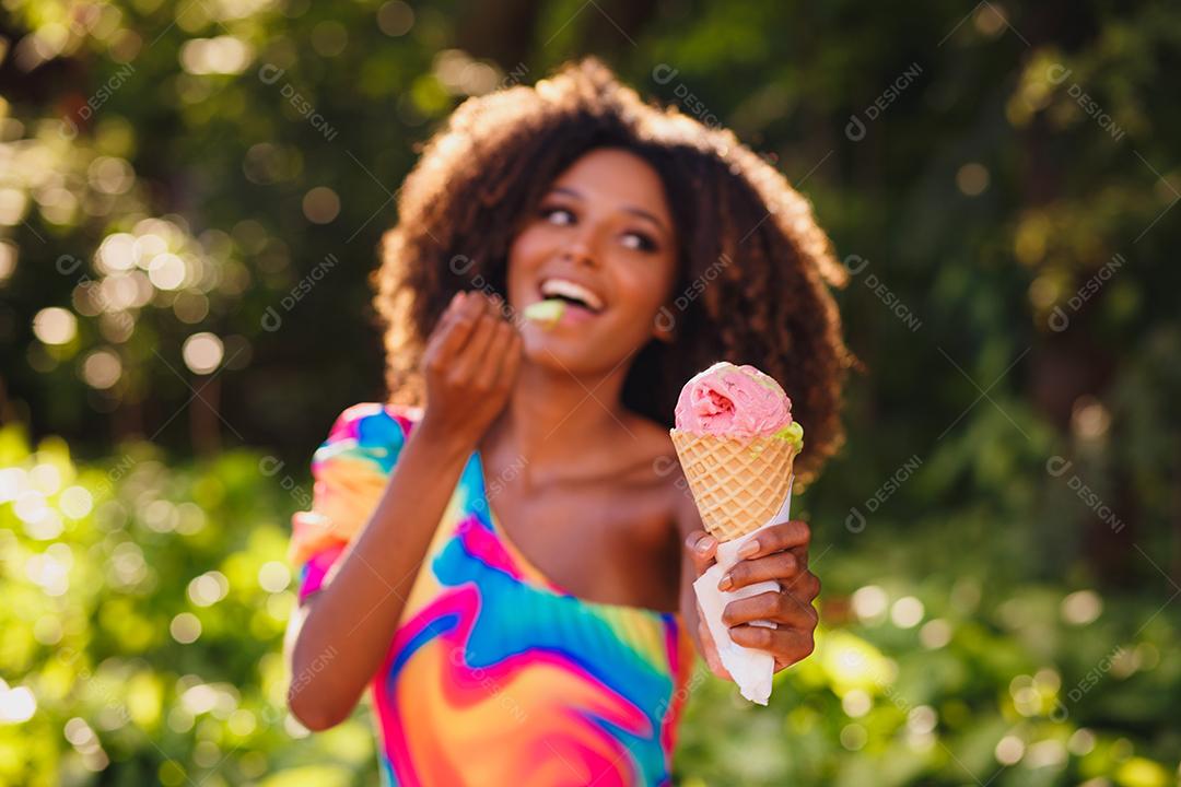 Mulher afro feliz tomando sorvete no parque.