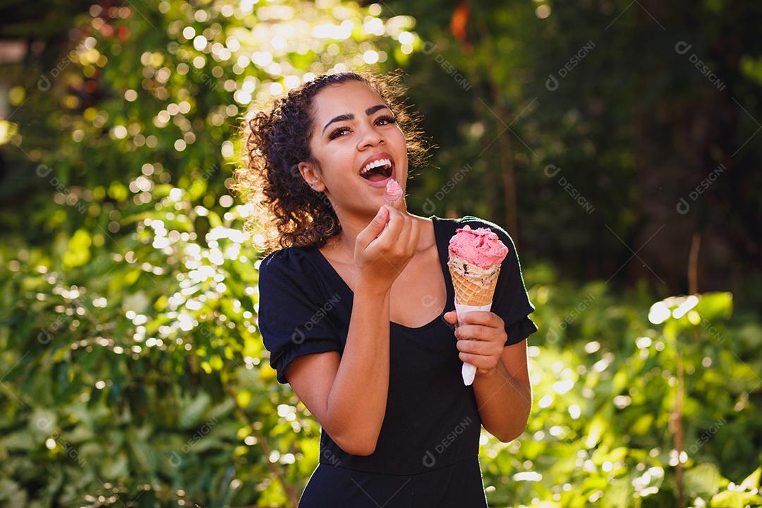 Mulher afro feliz tomando sorvete no parque.