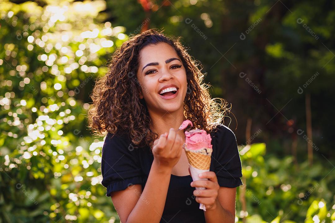 Mulher afro feliz tomando sorvete no parque.