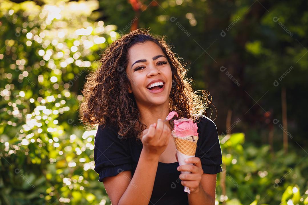 Mulher afro feliz tomando sorvete no parque.