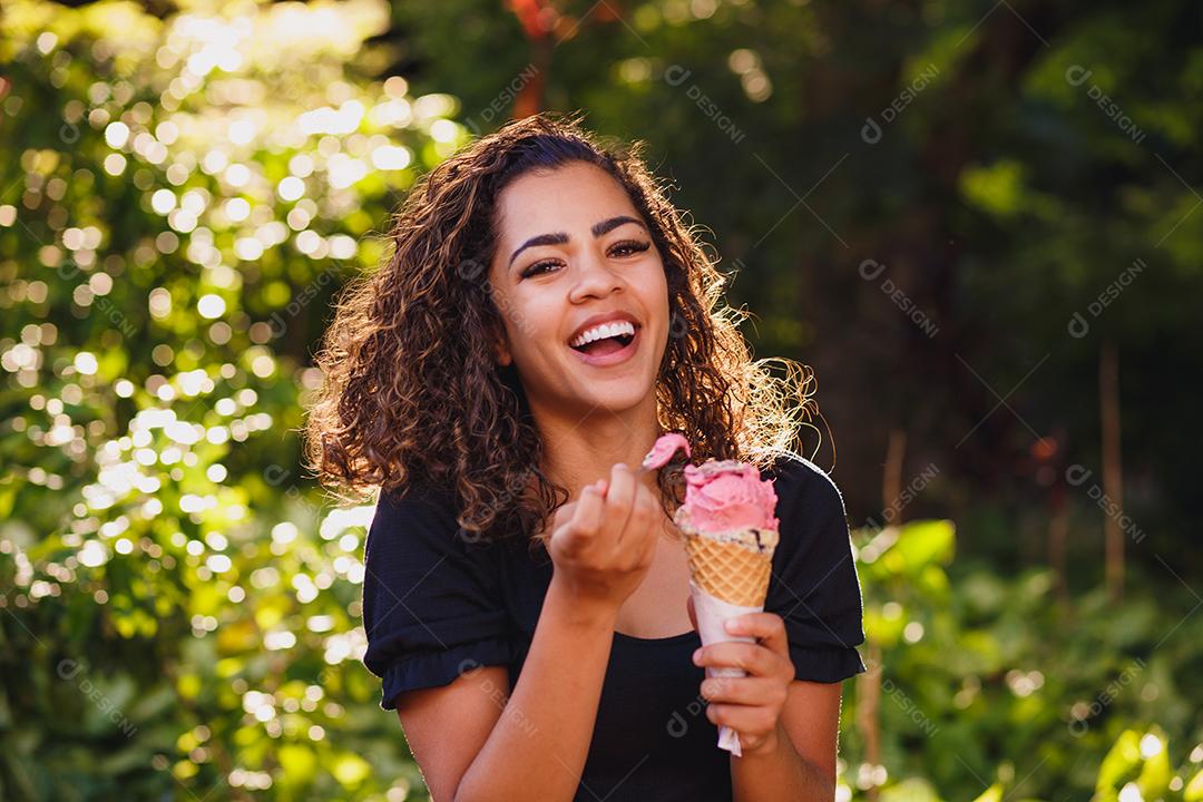 Mulher afro feliz tomando sorvete no parque.