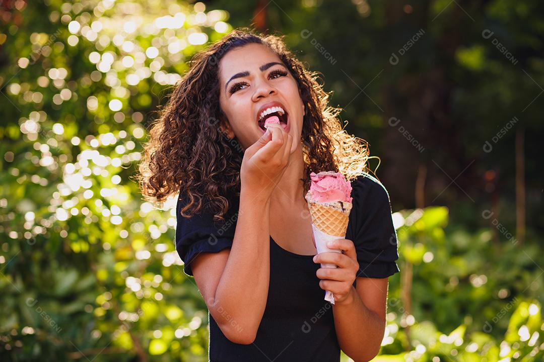 Mulher afro feliz tomando sorvete no parque.