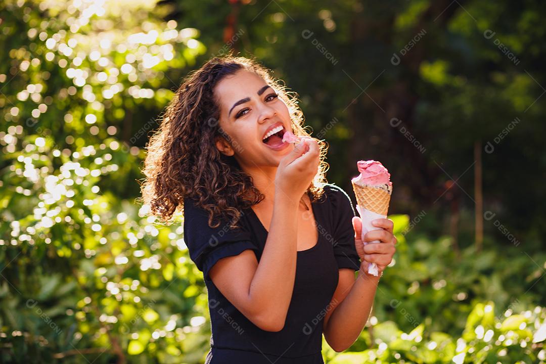 Mulher afro feliz tomando sorvete no parque.