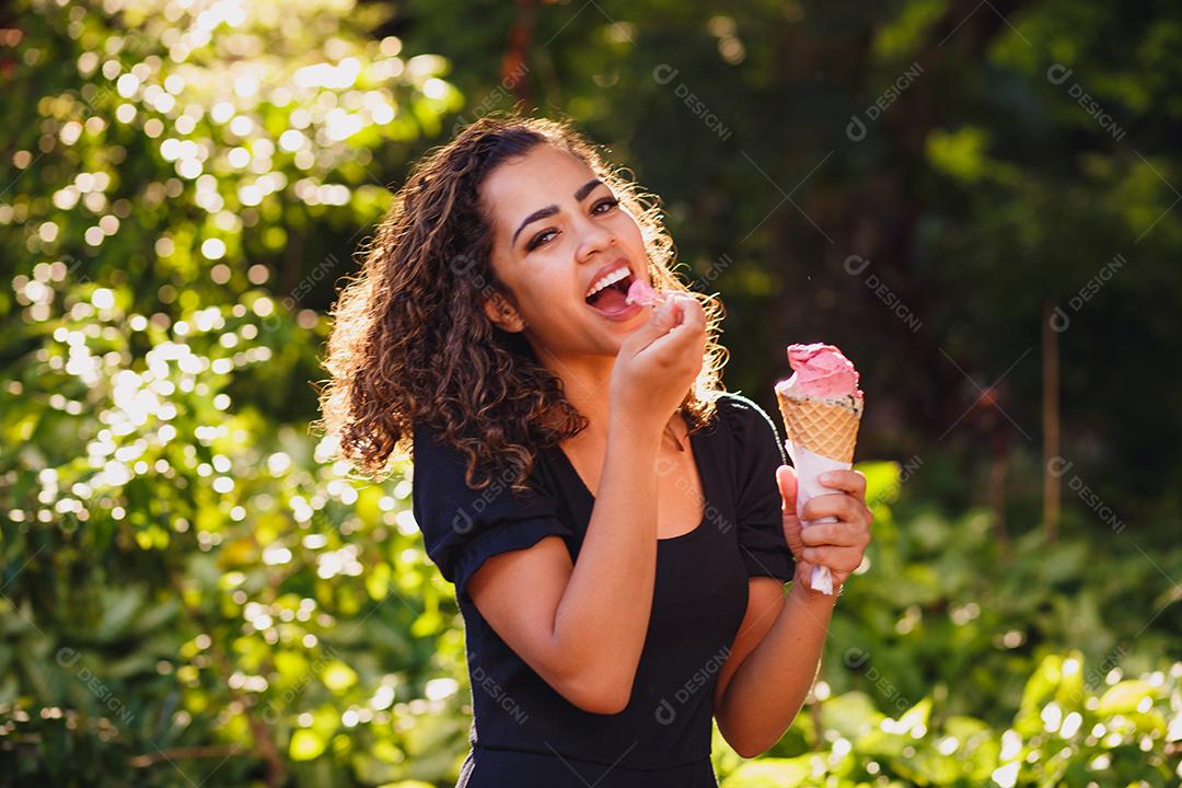 Mulher afro feliz tomando sorvete no parque.