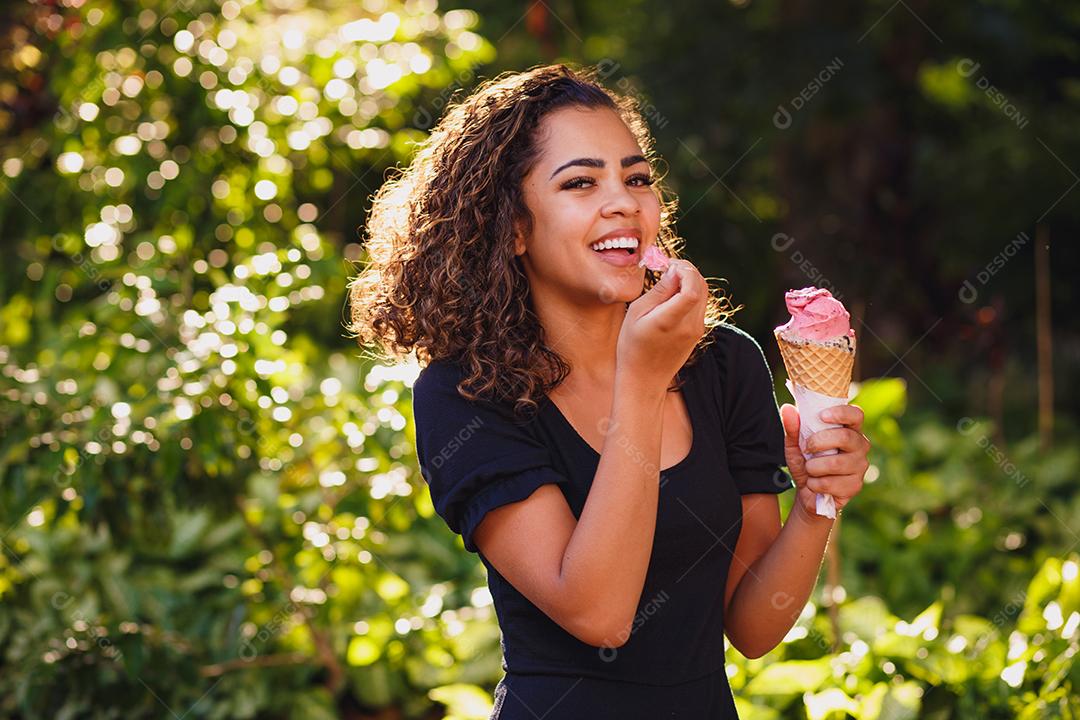 Mulher afro feliz tomando sorvete no parque.