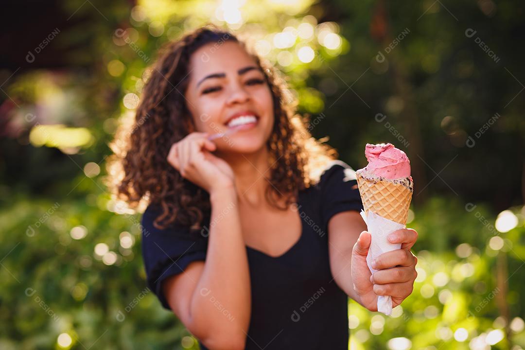 Mulher afro feliz tomando sorvete no parque.