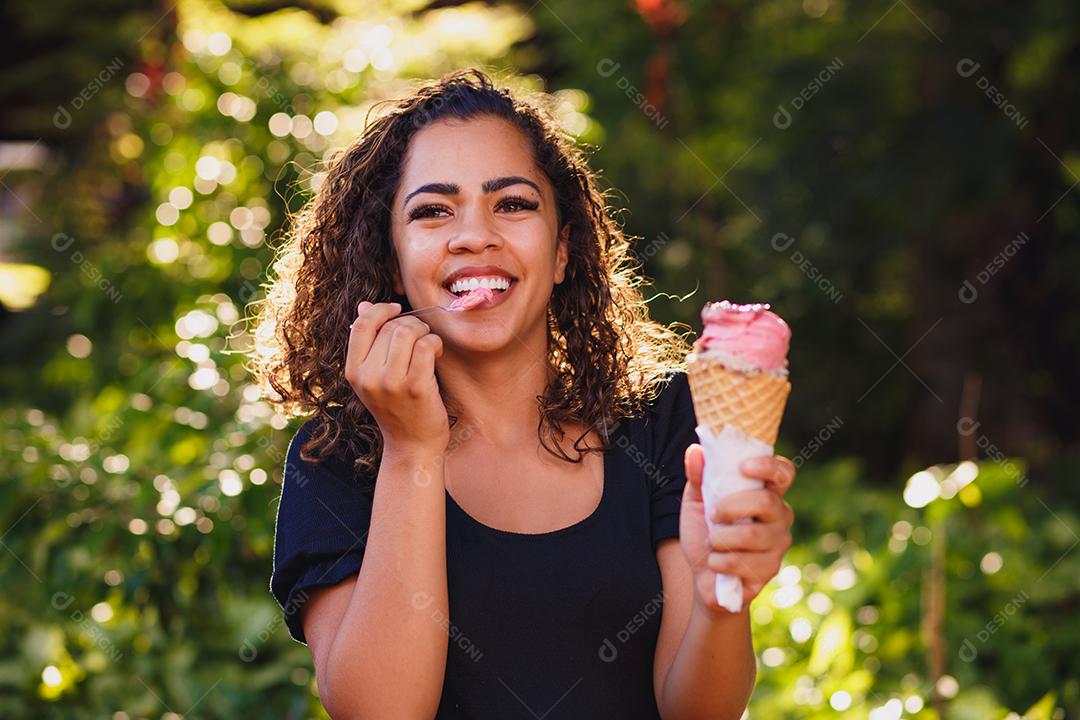 Mulher afro feliz tomando sorvete no parque.