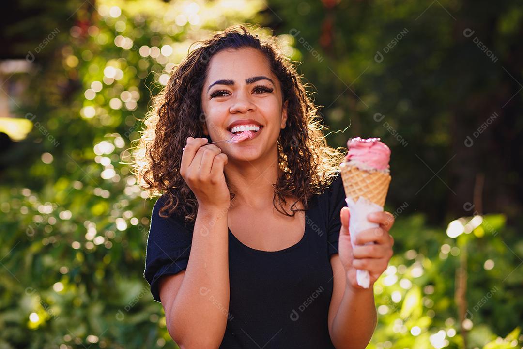 Mulher afro feliz tomando sorvete no parque.