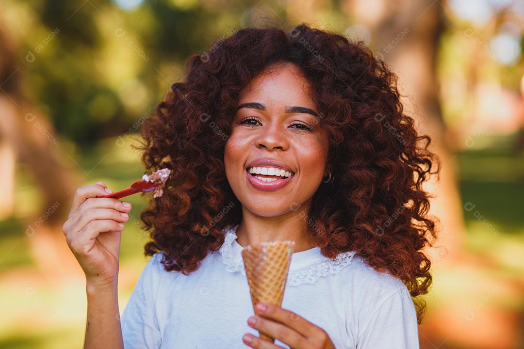 Mulher afro feliz tomando sorvete no parque.