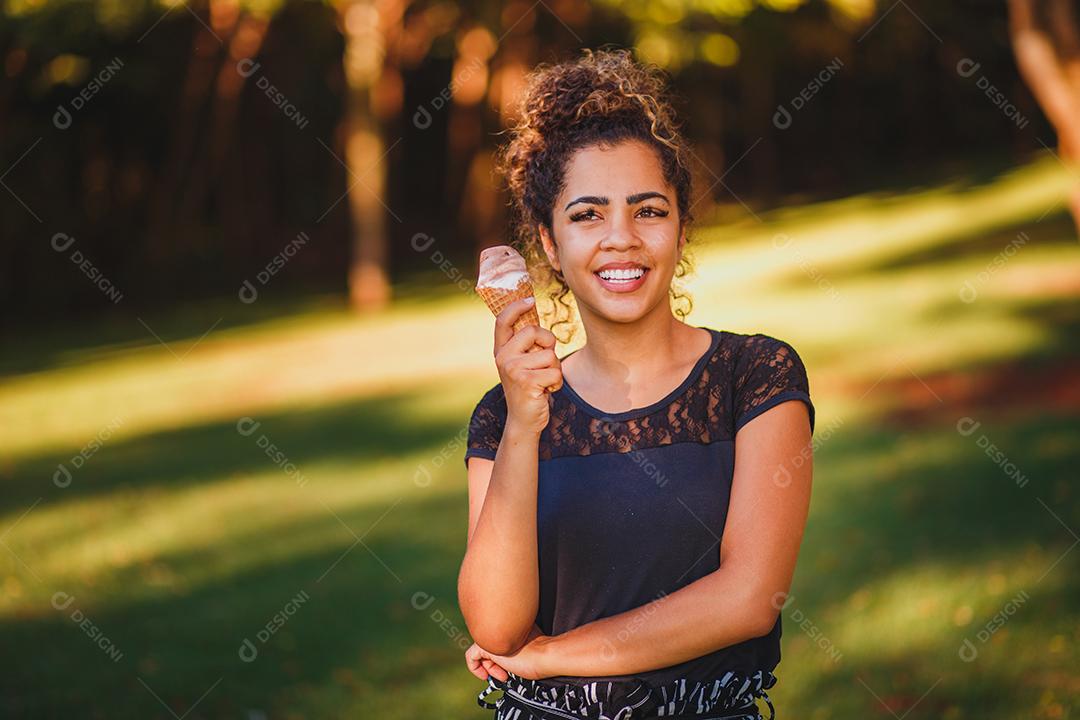 Mulher afro feliz tomando sorvete no parque.