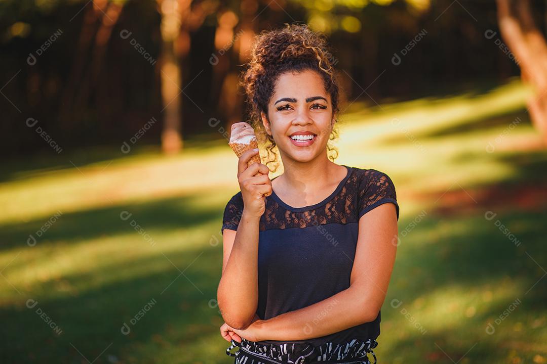 Mulher afro feliz tomando sorvete no parque.