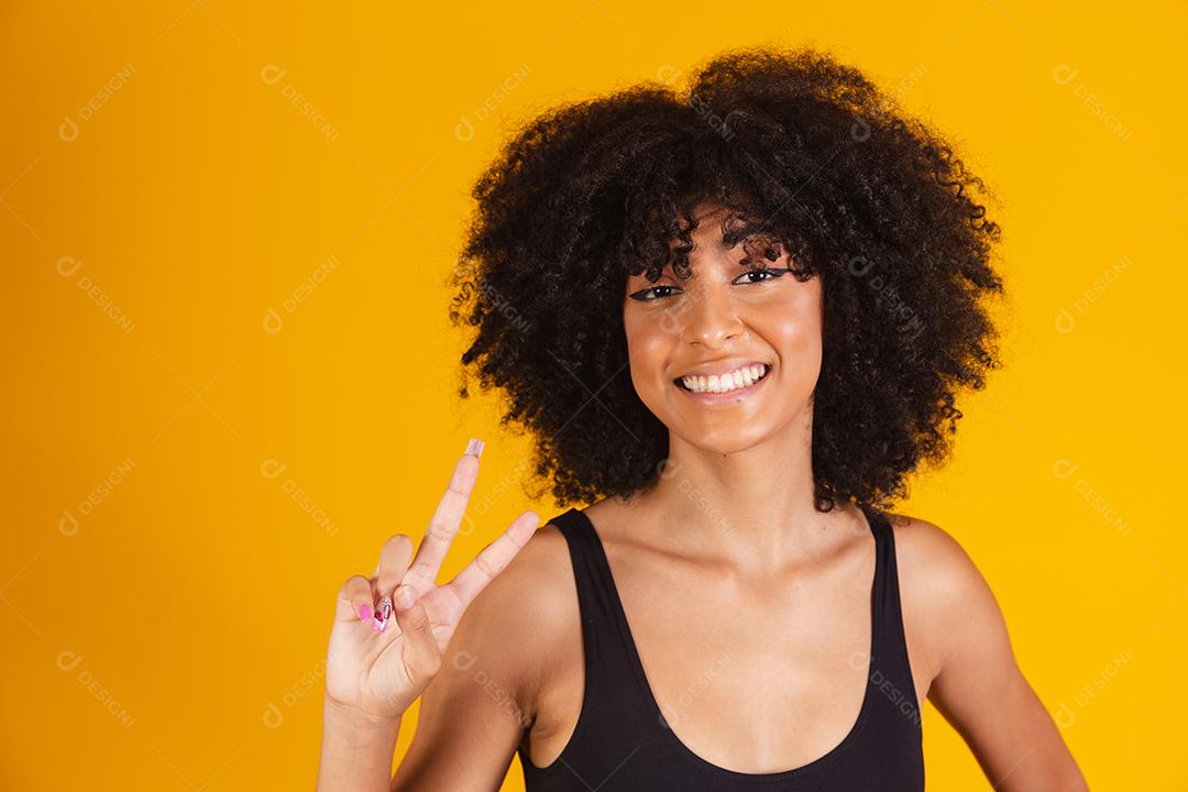 mulher afro fazendo sinal de V com as mãos. Garota afro feliz com boa vibração fazendo paz e amor com as mãos