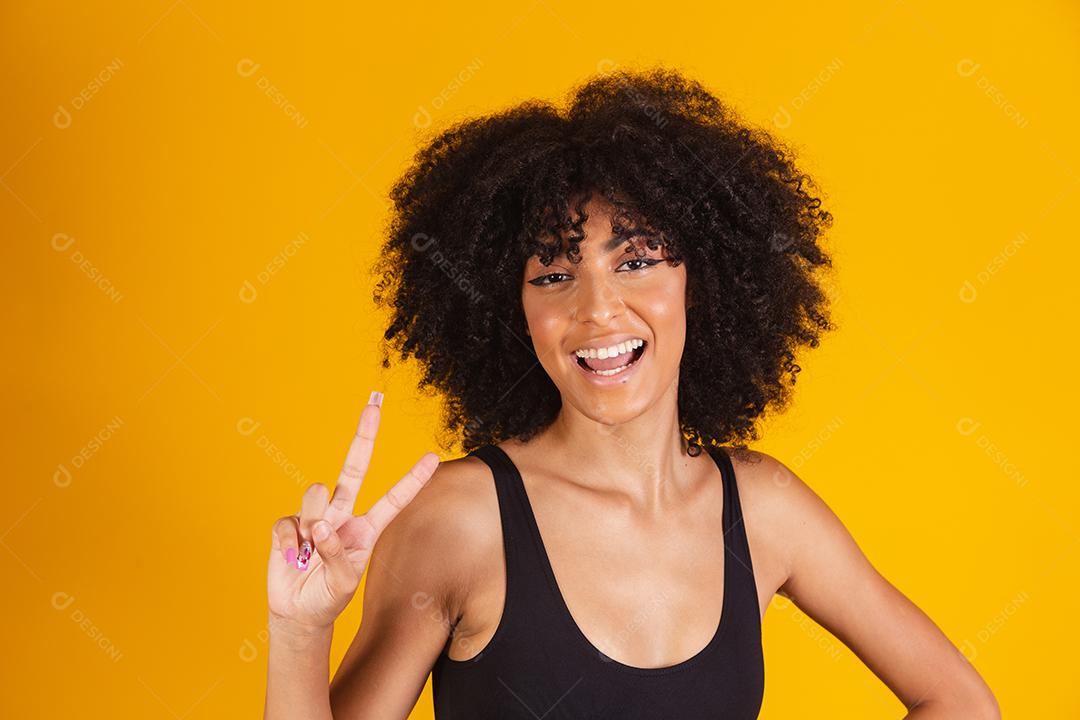 mulher afro fazendo sinal de V com as mãos. Garota afro feliz com boa vibração fazendo paz e amor com as mãos