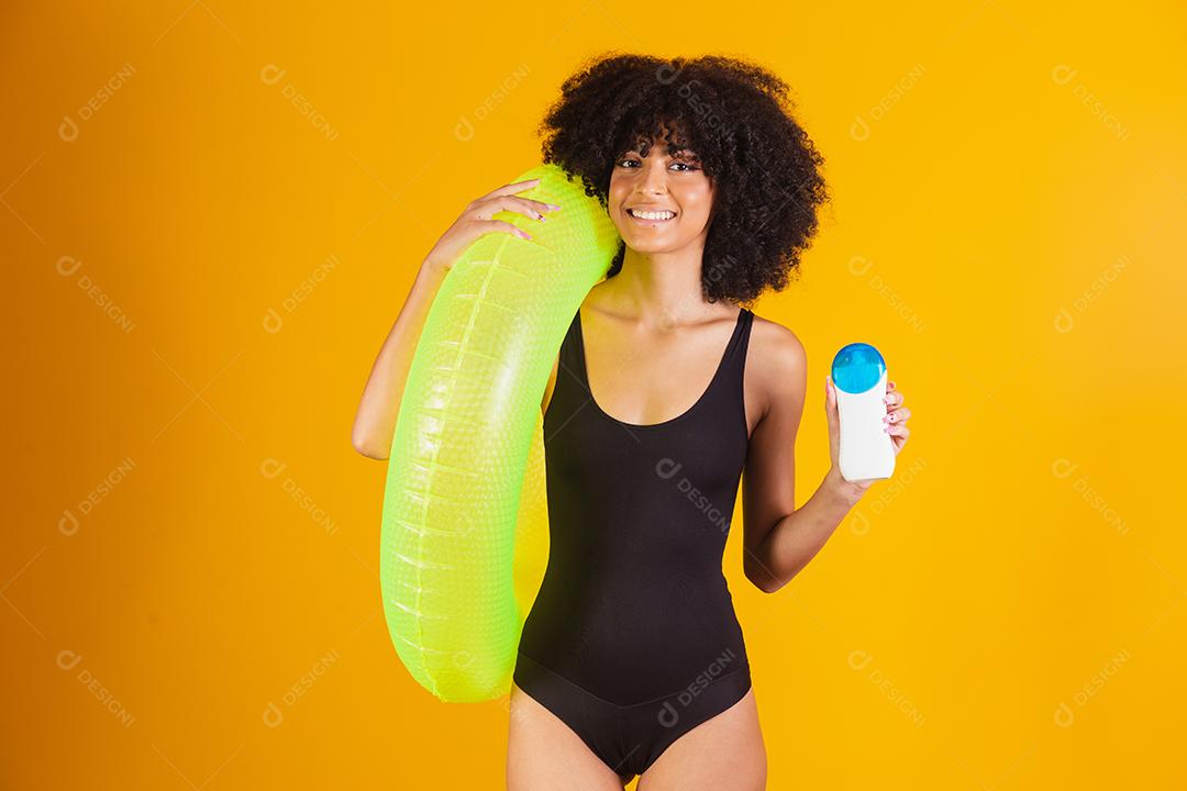 Mulher de férias segurando bóia flutuante e protetor solar em fundo amarelo