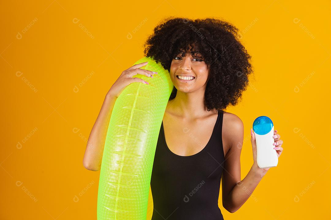 Mulher de férias segurando bóia flutuante e protetor solar em fundo amarelo