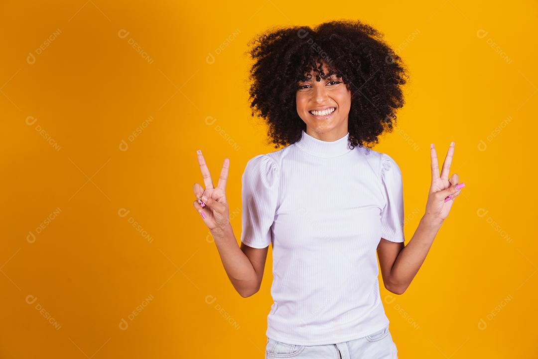 Jovem linda mulher afro-americana com cabelos cacheados, vestindo camiseta casual em pé sorrindo para a câmera