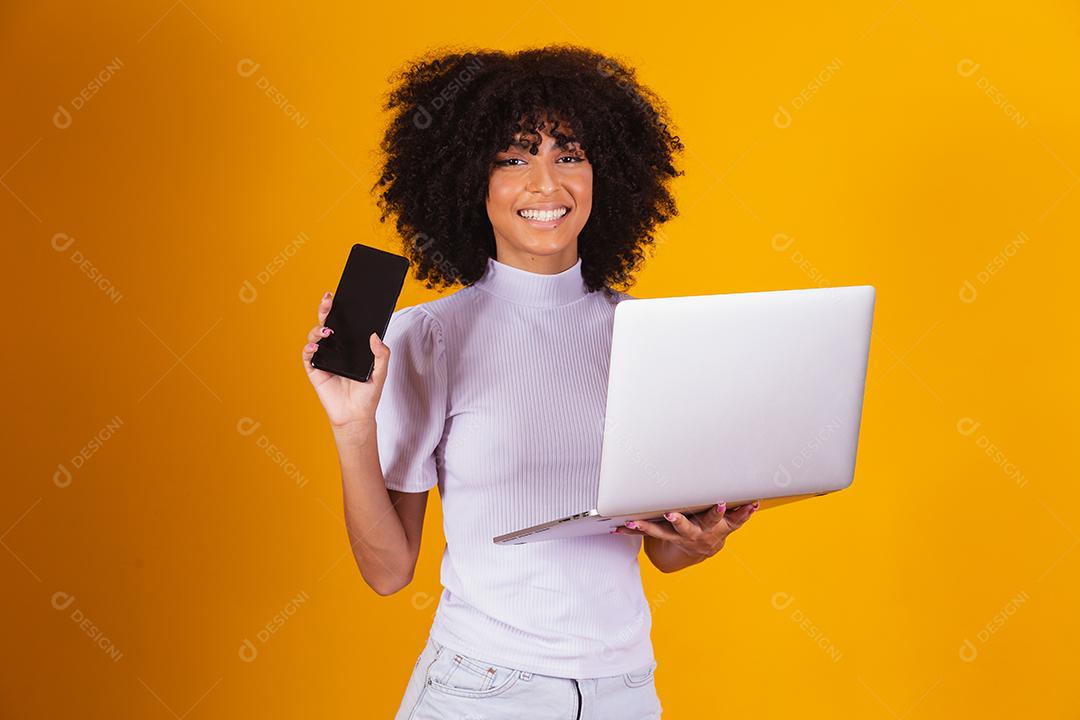 mulher afro segurando um celular na mão e a outra com um notebook