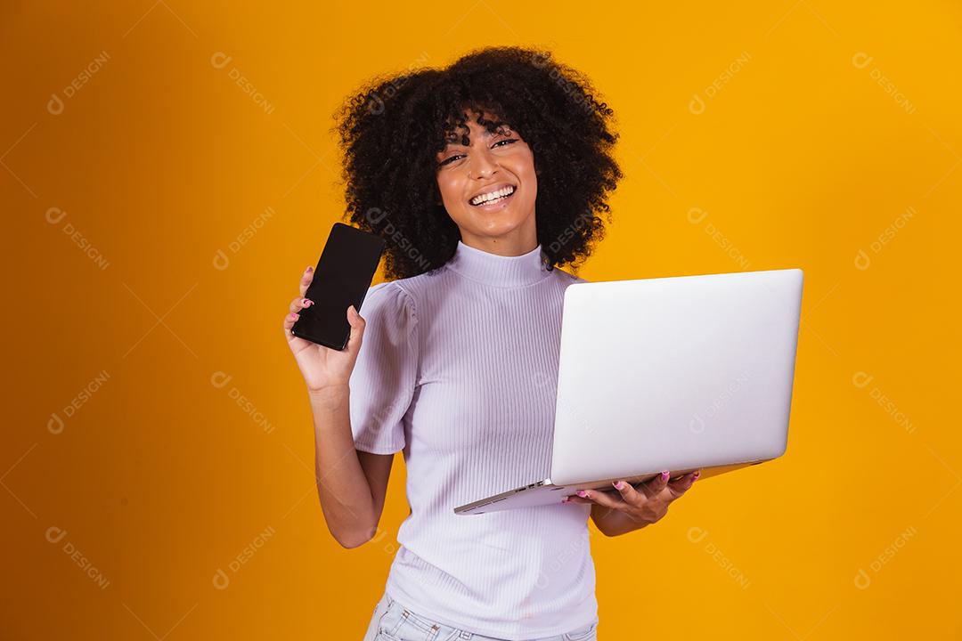 mulher afro segurando um celular na mão e a outra com um notebook