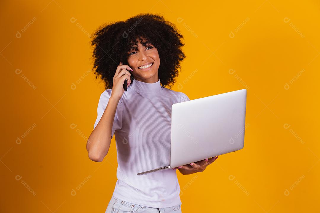 Mulher negra segurando um computador falando ao telefone