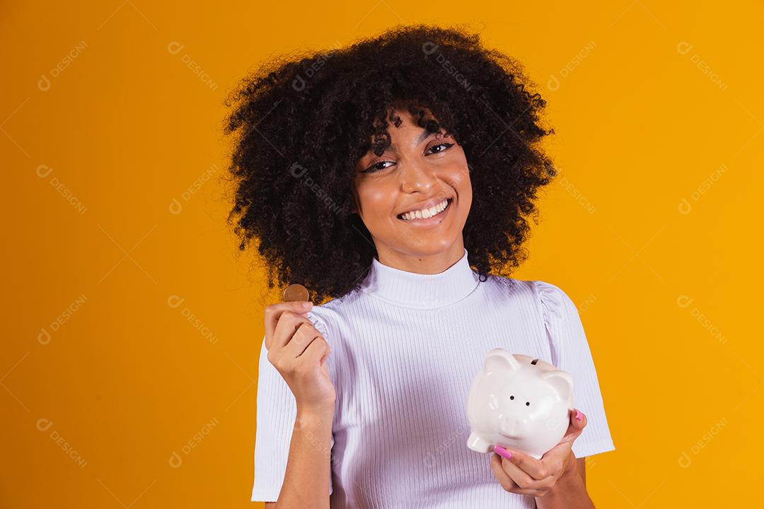 Mulher negra segurando um cofrinho. Mulher economizando dinheiro em porquinho