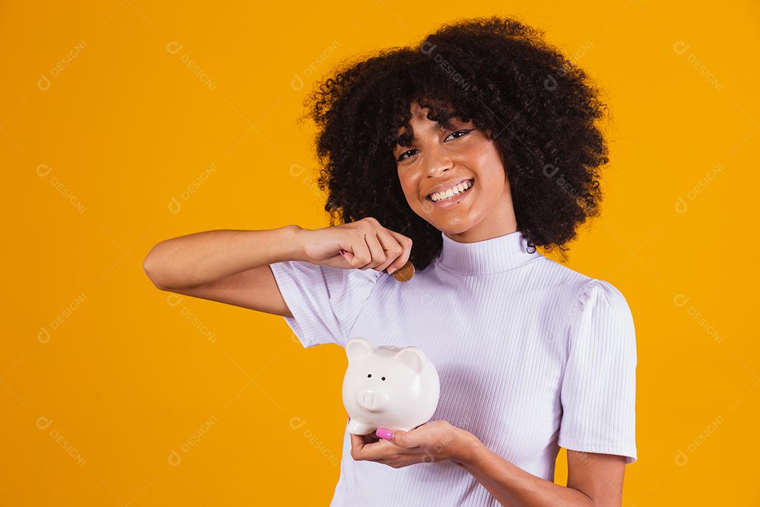 Mulher negra segurando um cofrinho. Mulher economizando dinheiro no porquinho