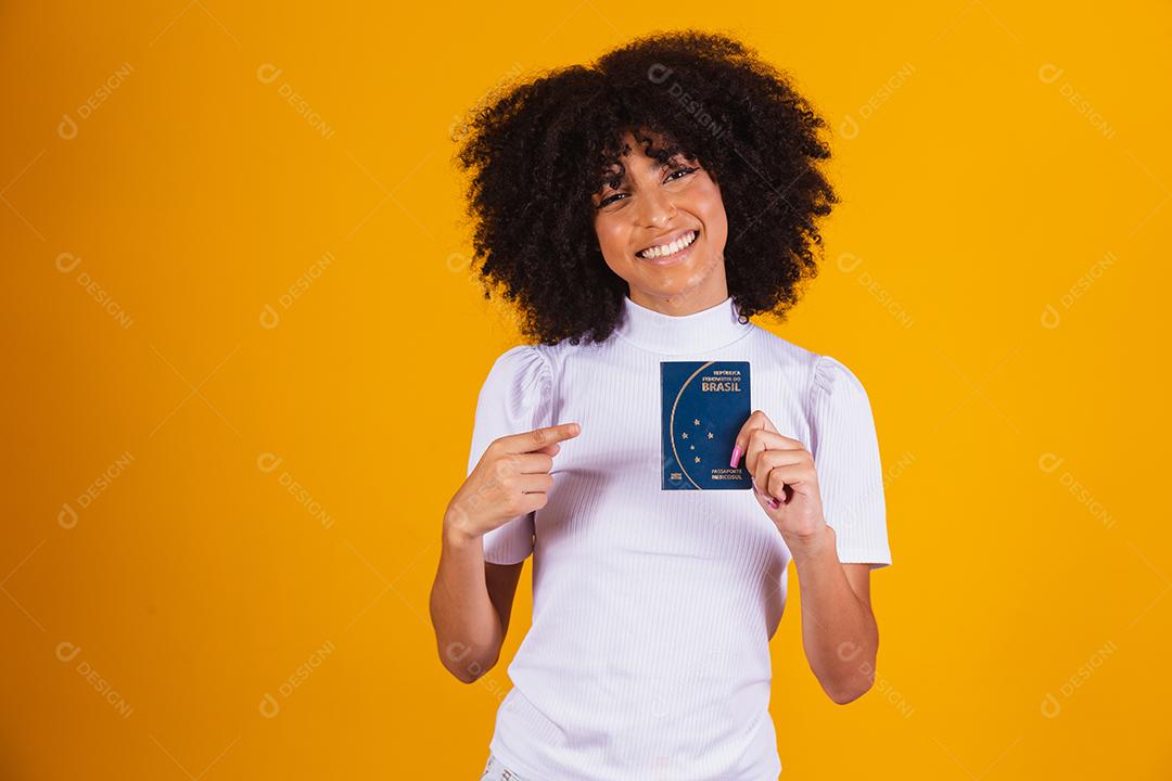 mulher afro segurando um passaporte brasileiro nas mãos.
