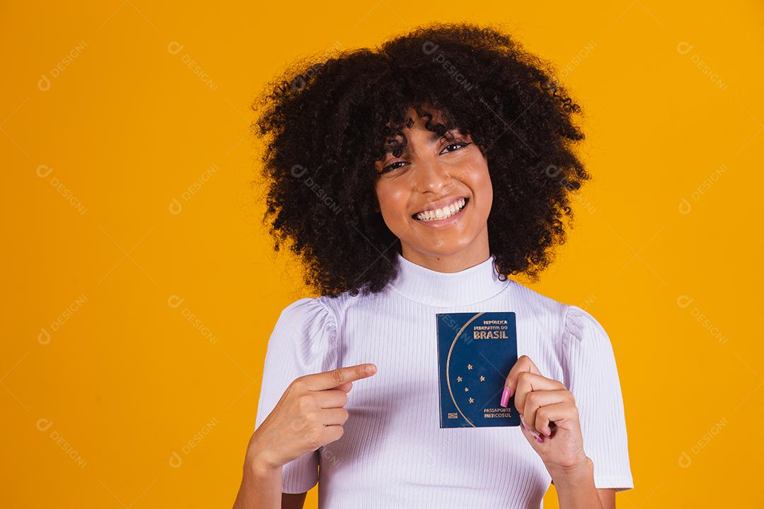 mulher afro segurando um passaporte brasileiro nas mãos.