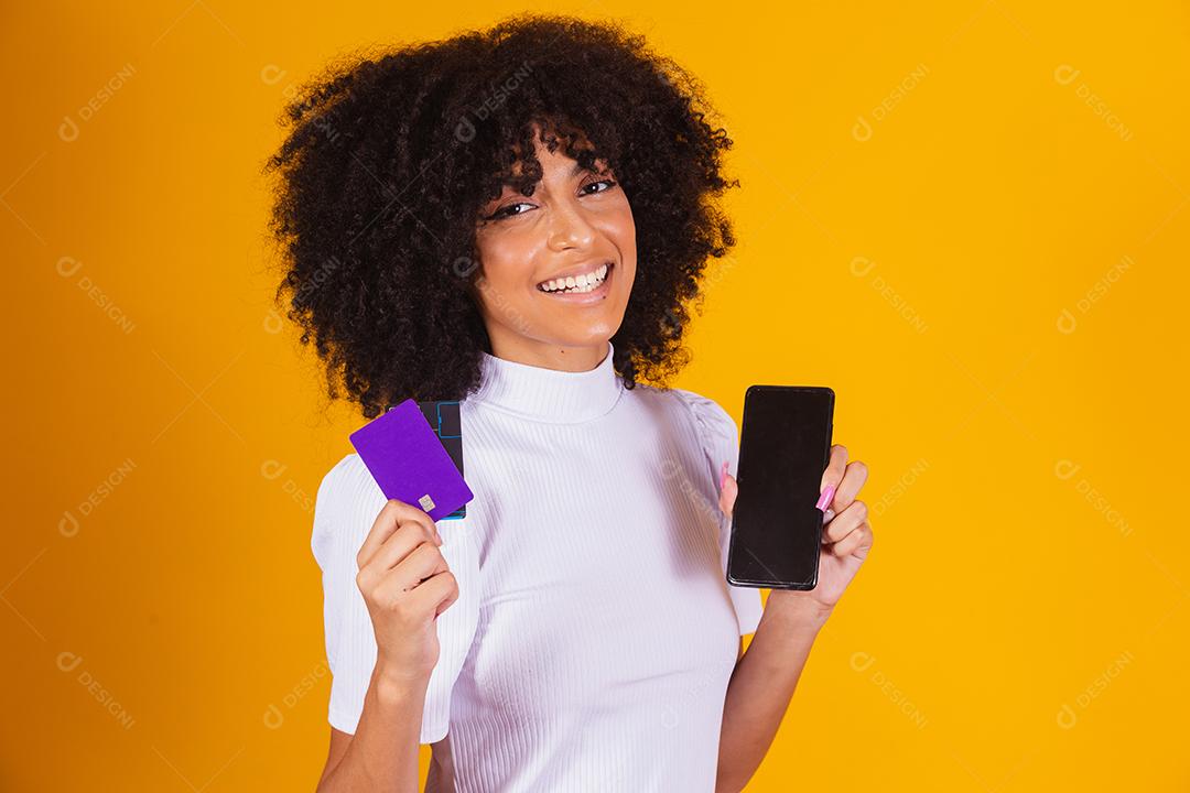 Foto de linda mulher de pele escura animada segurando cartão de crédito plástico mostrando novo modelo de telefone