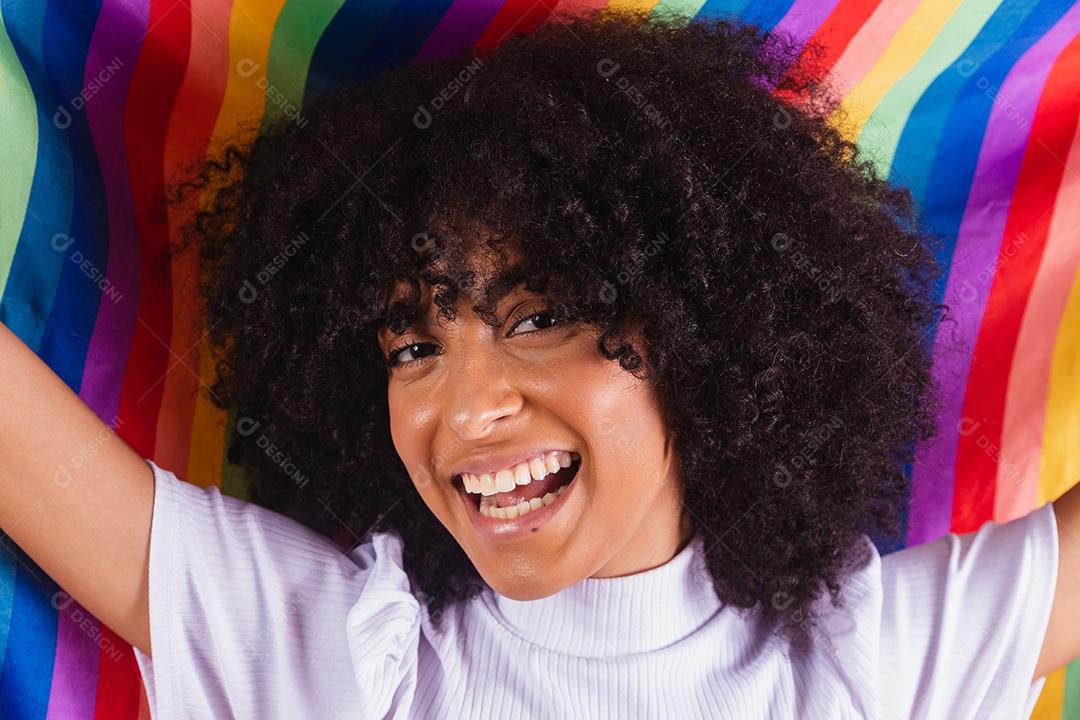 Mulher jovem de cabelo encaracolado cobrindo com a bandeira do orgulho lgbt. Sozinho. Um. Mantendo o punho erguido