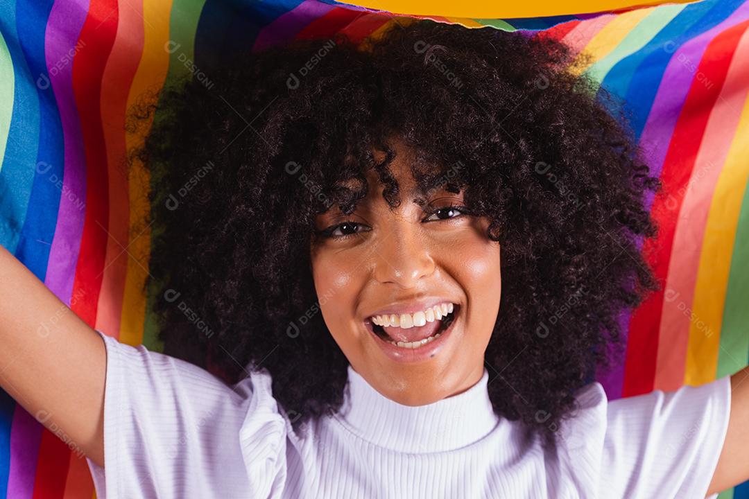 Mulher jovem de cabelo encaracolado cobrindo com a bandeira do orgulho lgbt. Sozinho. Um. Mantendo o punho erguido