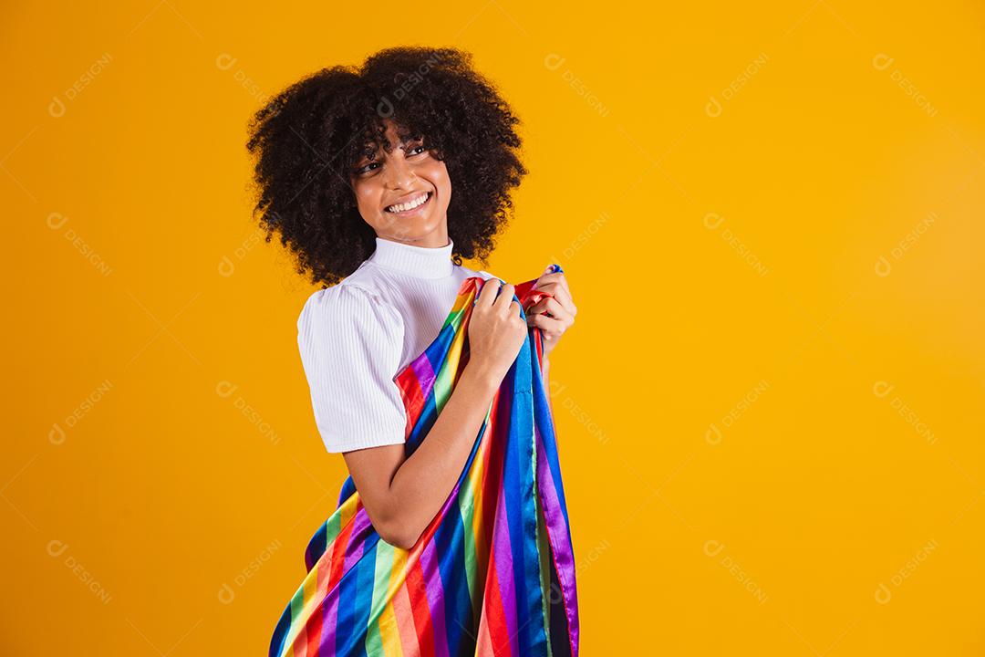 Mulher jovem de cabelo encaracolado cobrindo com a bandeira do orgulho lgbt. Sozinho. Um. Mantendo o punho erguido
